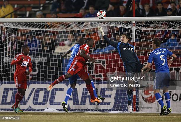 Fabian Castillo of FC Dallas looks on as Troy Perkins of Montreal Impact jumps for the save against Hendry Thomas of FC Dallas at Toyota Stadium on...