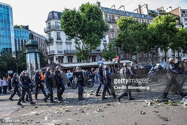 Riot police walk over broken glass bottles and debris littering a road as French cab drivers protest against Uber Technologies Inc.'s car sharing...
