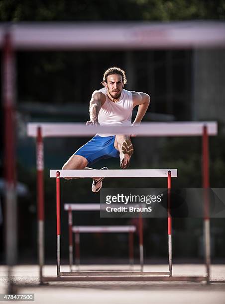 young determined athlete jumping hurdles on a race. - hordelopen atletiekonderdeel stockfoto's en -beelden