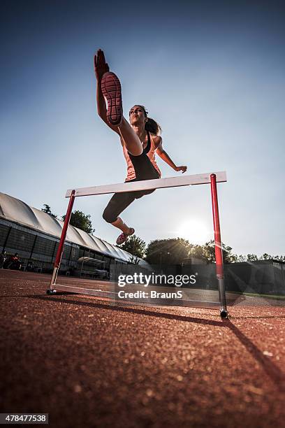 below view of a young woman jumping hurdle. - hurdle stock pictures, royalty-free photos & images
