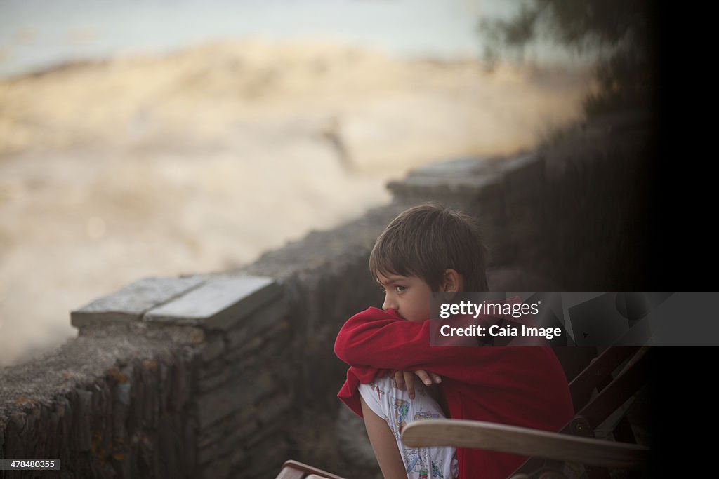 Pensive boy sitting along rock wall