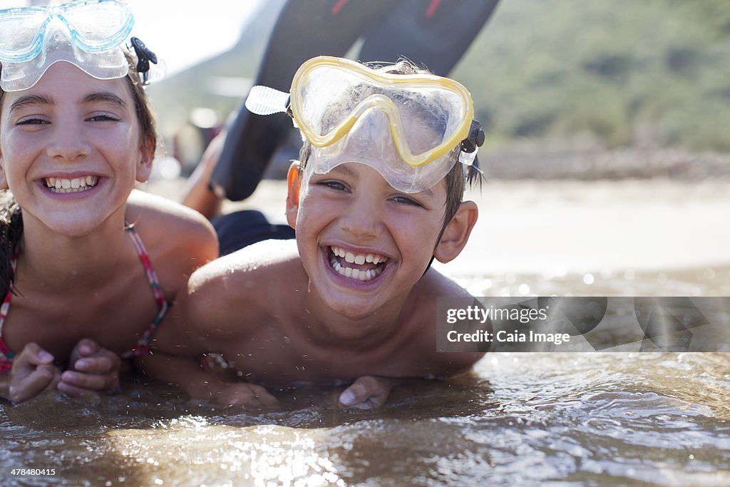 Enthusiastic brother and sister wearing goggles and laying in ocean