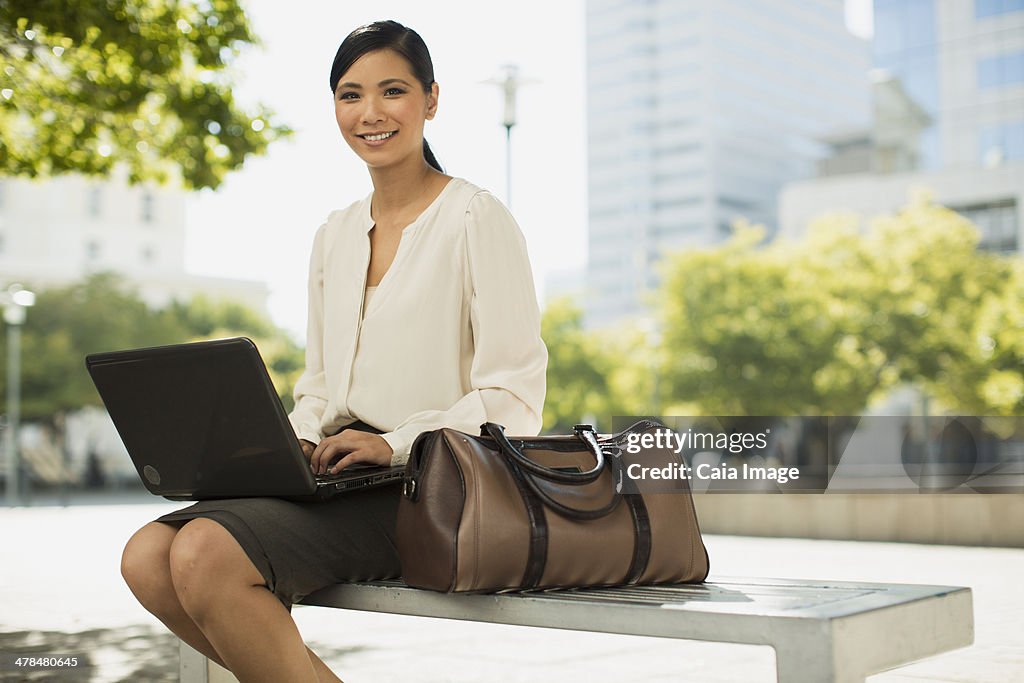 Smiling businesswoman sing laptop in urban park