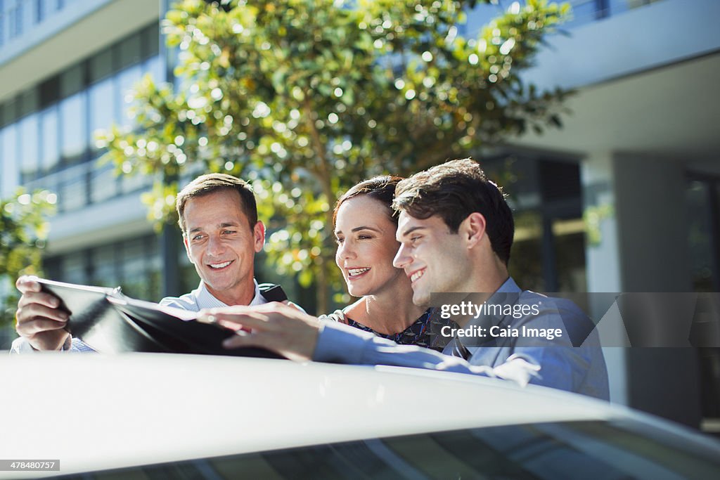 Business people looking at paperwork on top of car