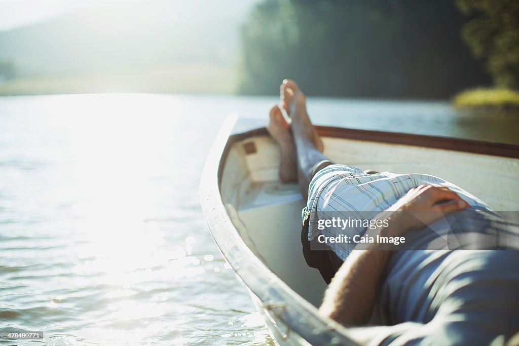 Man laying in rowboat on tranquil lake