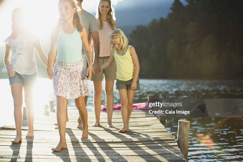 Family holding hands and walking on dock over lake