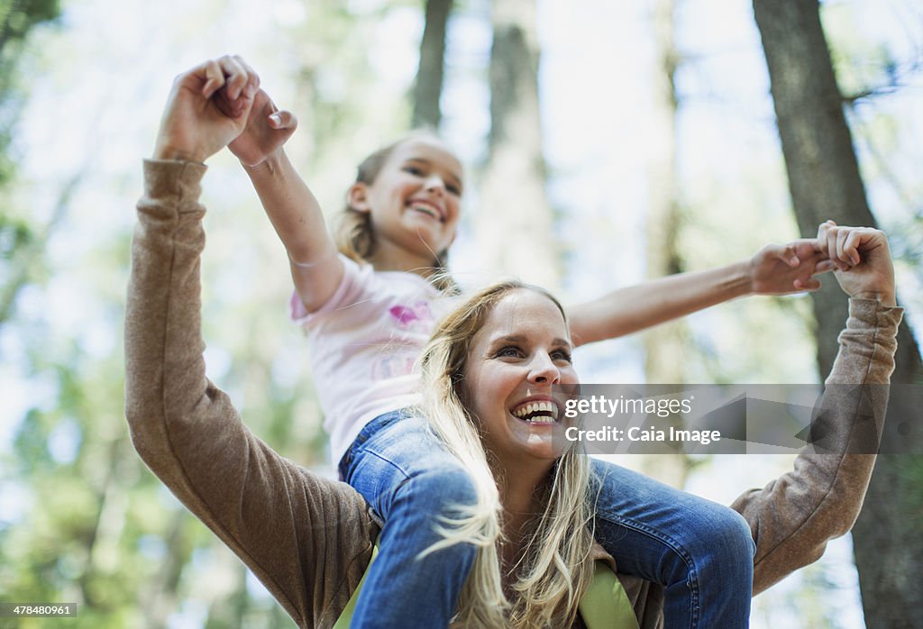 Mother carrying daughter on shoulders in woods