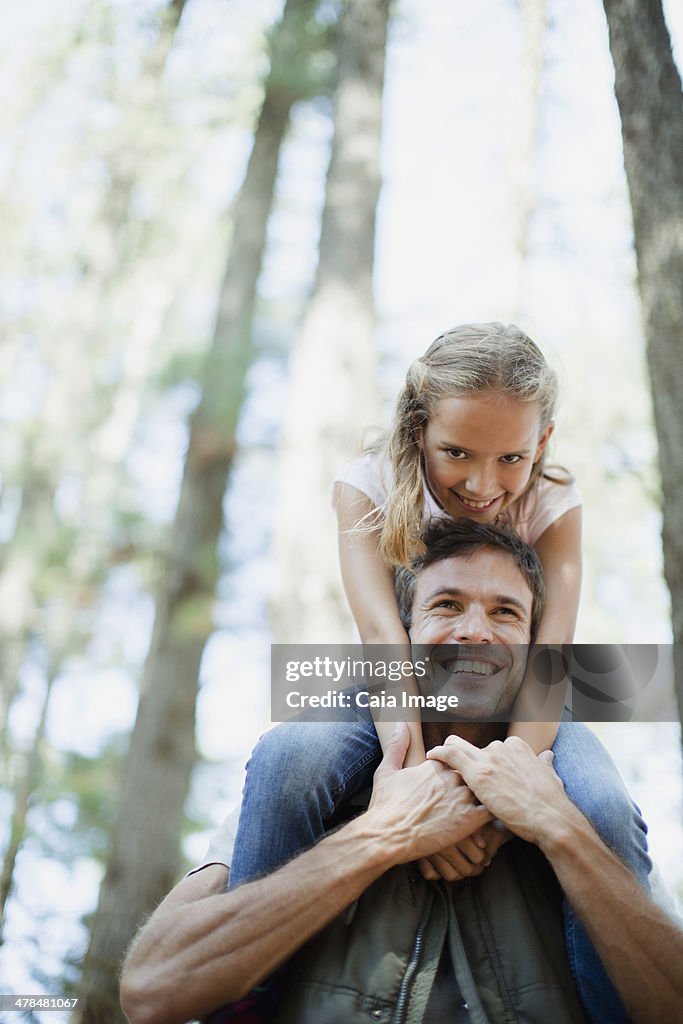 Smiling father carrying daughter on shoulders in woods