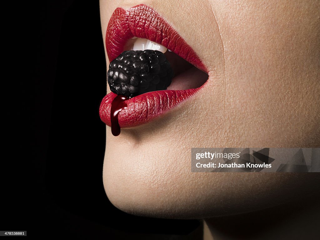 Female with red lipstick biting blackberry, close