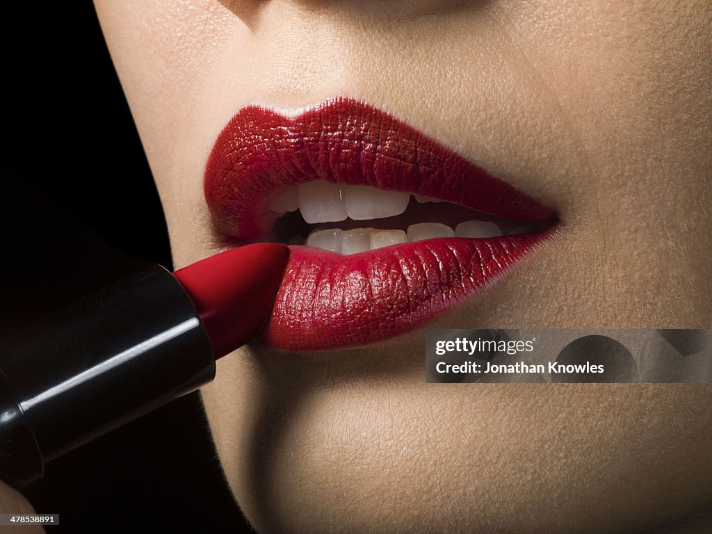 Female applying red lipstick, close up