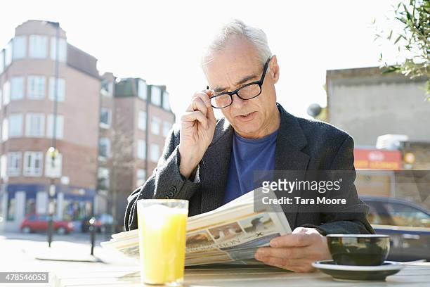 senior man reading newspaper at cafe - leesbril stockfoto's en -beelden