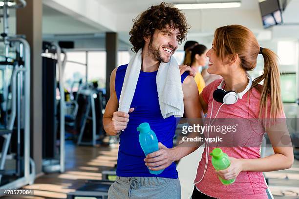 young smiling couple in a gym with towel around neck. - headphone man on neck stockfoto's en -beelden