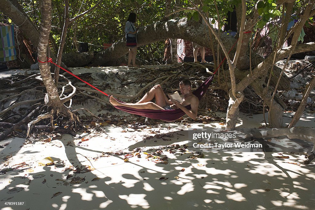 A tourist reads in a hammock at his beachfront campsite in...