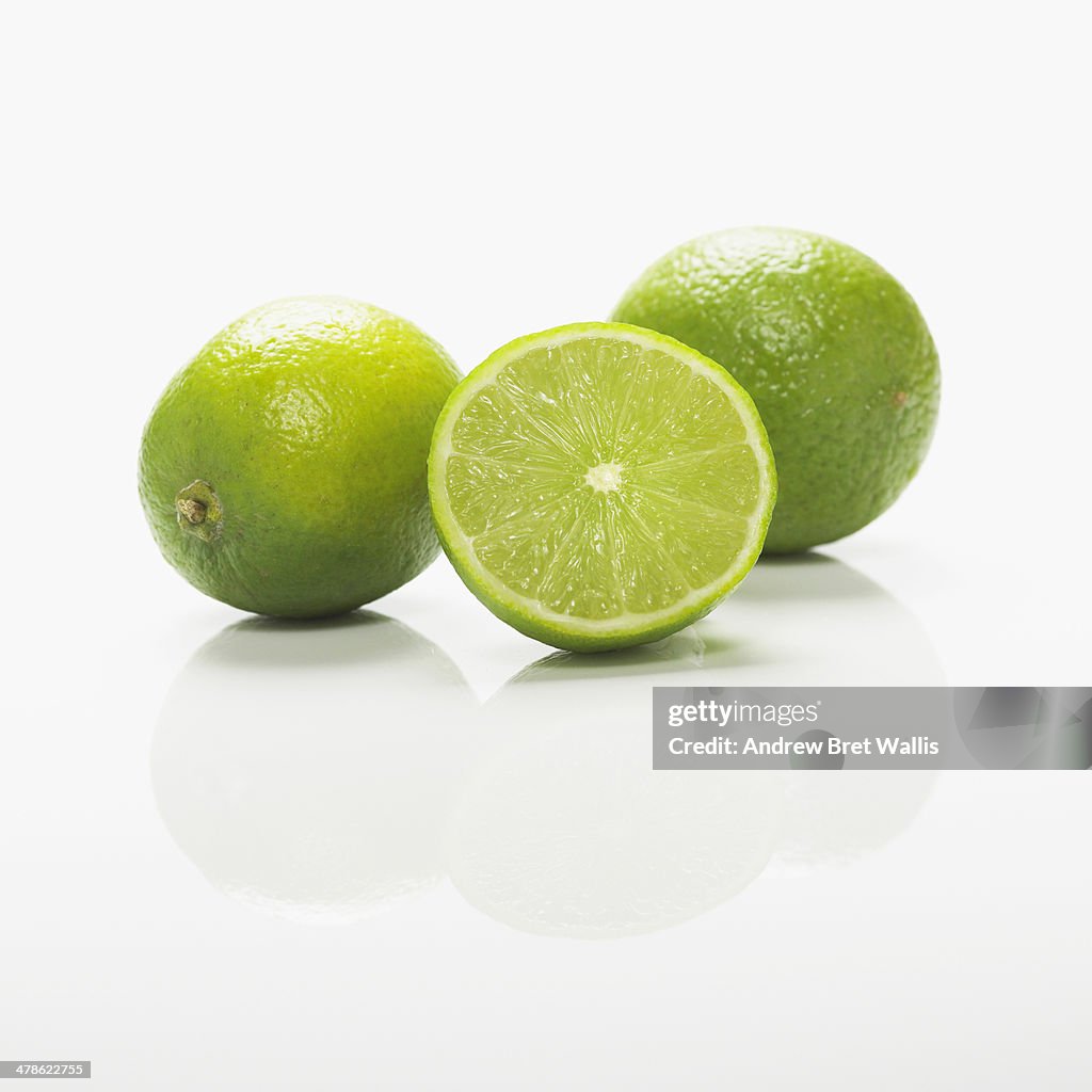 Whole and sliced fresh limes against white