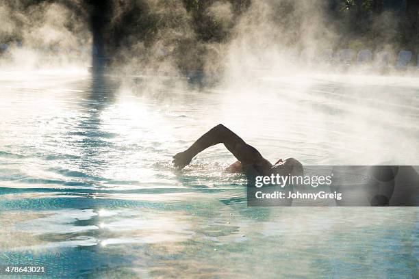 silhouette of man swimming as steam rides from pool - stoom stockfoto's en -beelden