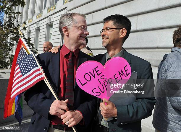John Lewis, left, and his husband Stuart Gaffney, plaintiffs in the 2008 Defense of Marriage Act case, hold flags and a sign reading "Love is...
