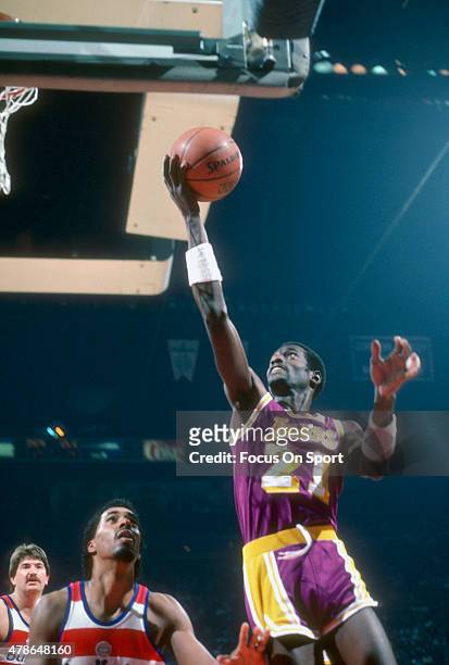 Michael Cooper of the Los Angeles Lakers goes up for a layup over Cliff Robinson of the Washington Bullets during an NBA basketball game circa 1984...