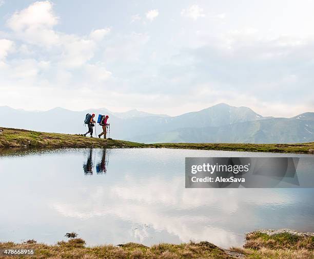 trekkers passing by a calm lake in the mountains - wandelen stockfoto's en -beelden