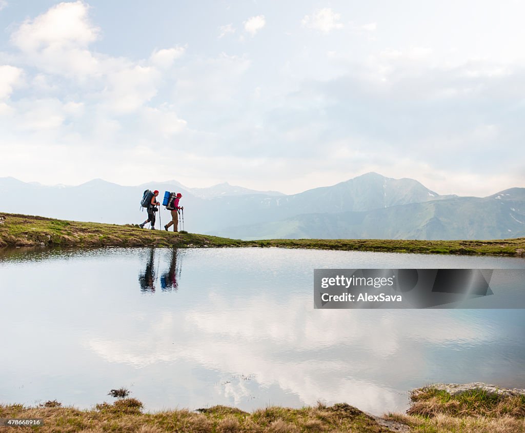 Trekkers passing by a calm lake in the mountains