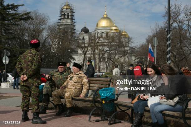 Cossacks volunteers and Simferopol residents sit on benches in a park next to Crimea's regional parliament building, in Simferopol, on March 14,...