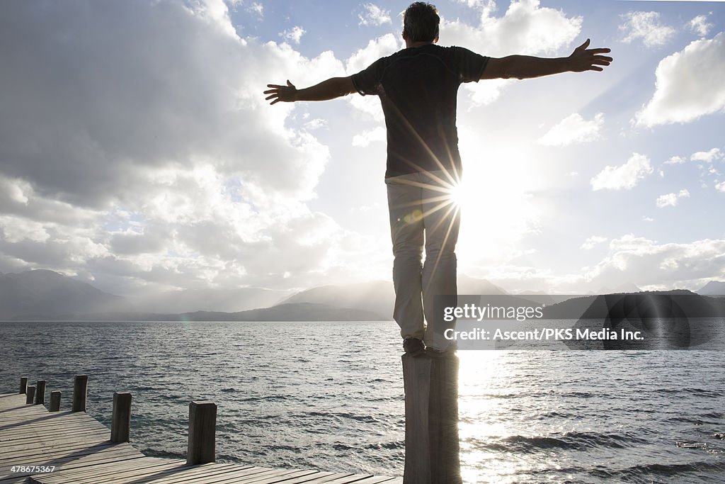 Man stands on wharf post, arms outstretched