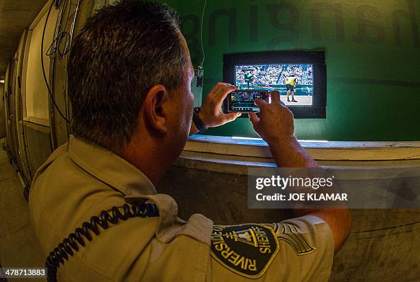 Officer David Wright of the Riverside Sheriff's department takes some snaps through a photographers' hole of the men's semifinal doubles between...