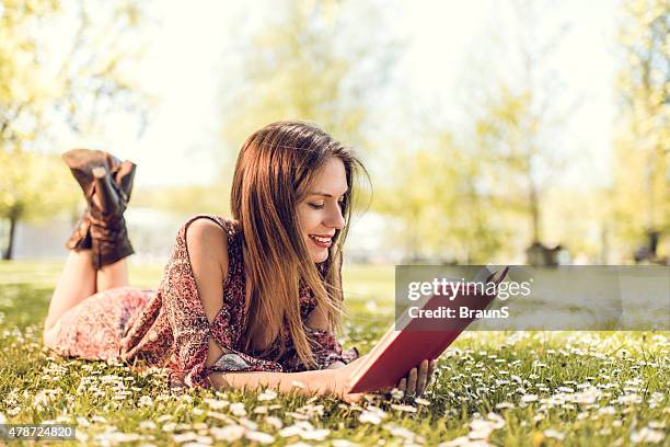 mujer sonriente descansando en la hierba leyendo un libro. - mujer leyendo libro en el parque fotografías e imágenes de stock