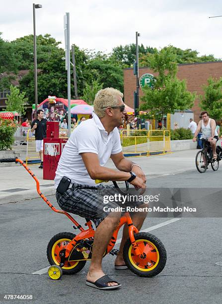 Salsa on St. Saint Clair Festival Scenes: A blond man riding a miniature bicycle with training wheels seems unaware of how silly he looks. His large...