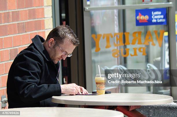 Man playing OLG scratching games in Toronto: Man with glasses sitting at an outdoor table in a cafe.
