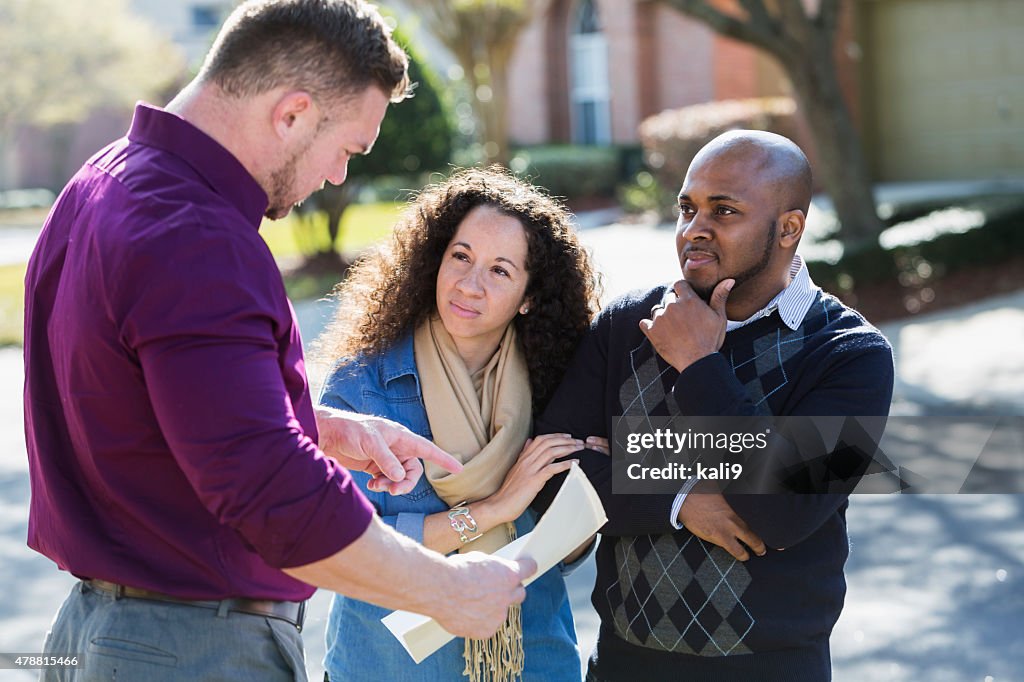 Black couple standing on residential street with agent