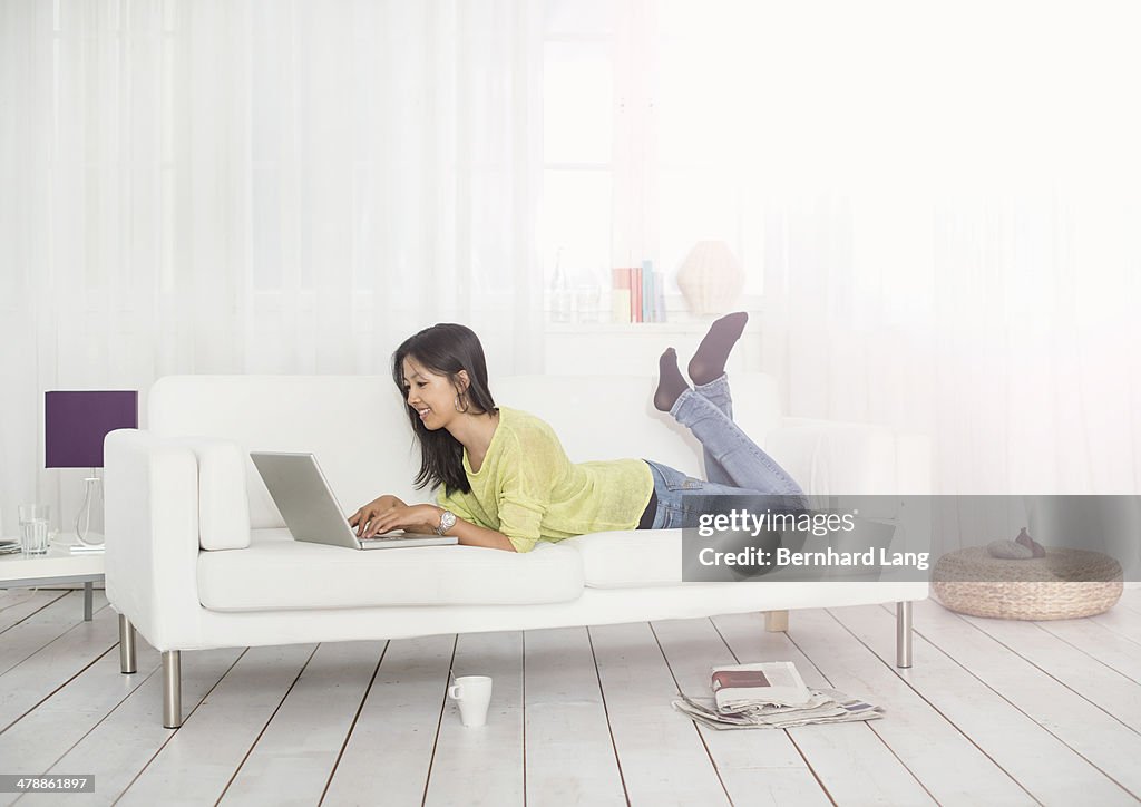 Young woman lying on sofa with laptop computer