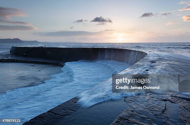 wave washing over sea wall at sunrise - argine diga foto e immagini stock