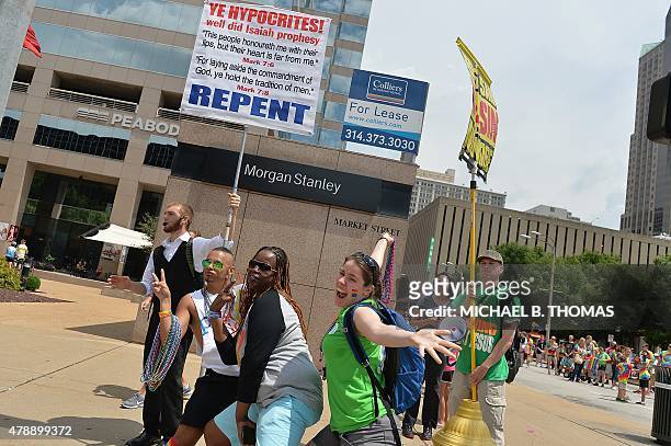 Gay pride parade participants pose as religious supporters protest in the background during the annual PrideFest parade in St. Louis, Missouri on...