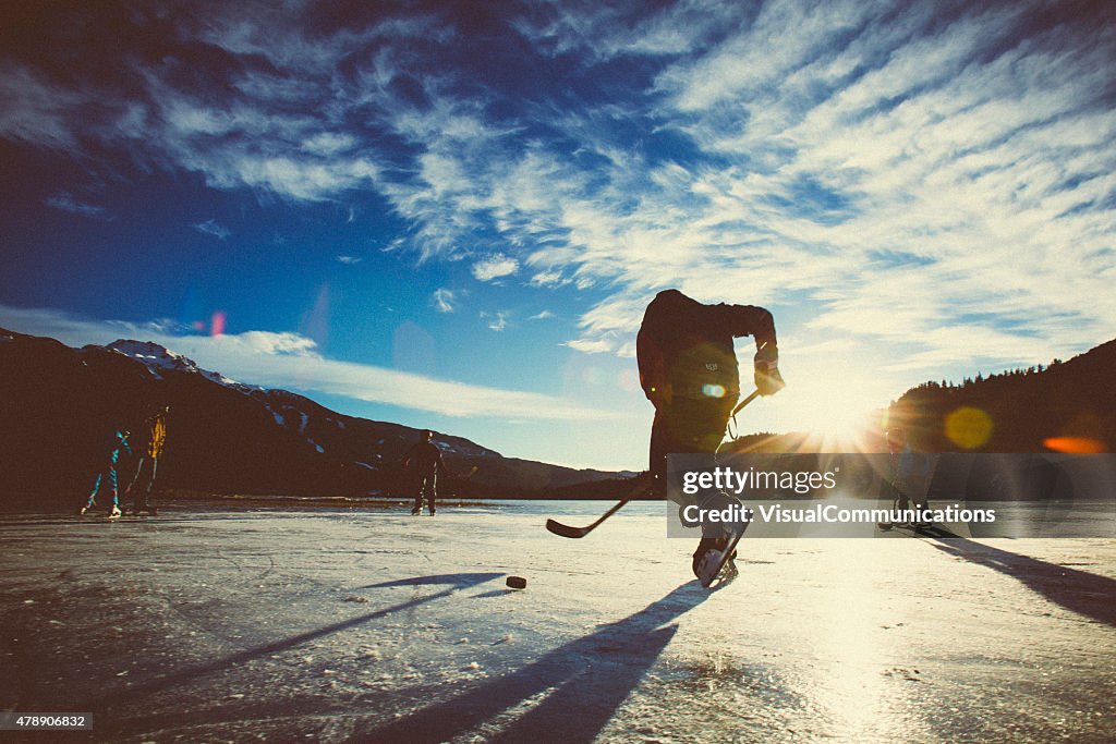 Playing ice hockey on frozen lake in sunset.