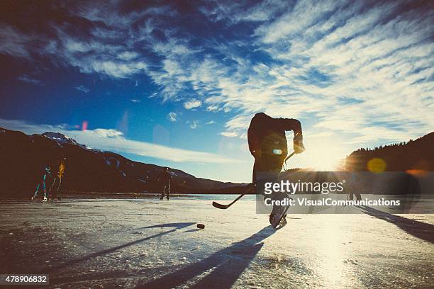 playing ice hockey on frozen lake in sunset. - ijshockeystick stockfoto's en -beelden