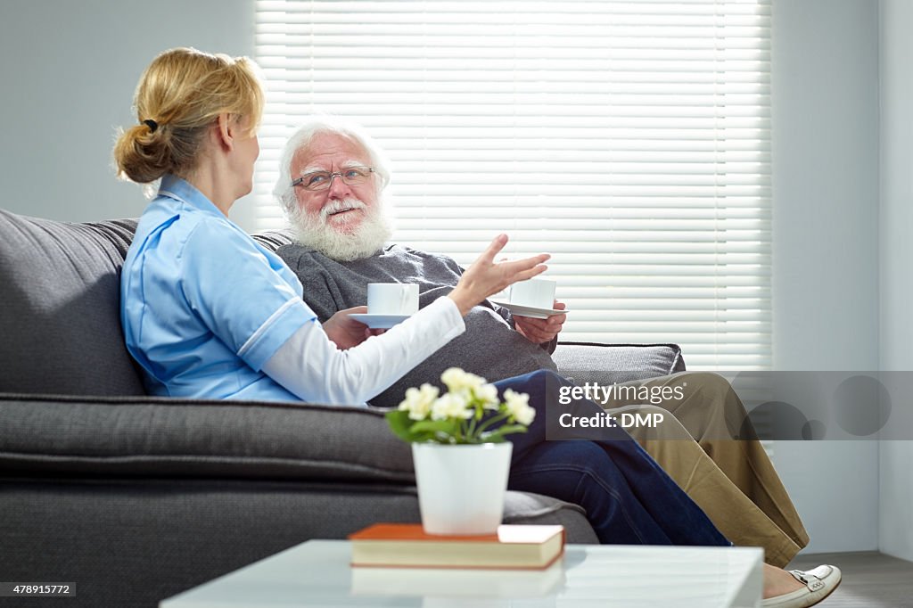 Home caregiver talking with senior man while sitting on sofa