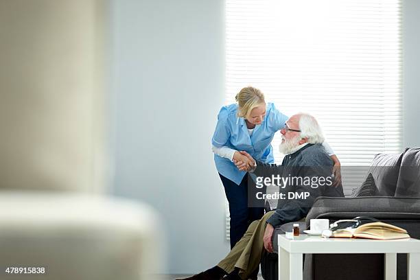 femmina caregiver aiutando uomo anziano alzarsi dal divano - servizio sociale foto e immagini stock