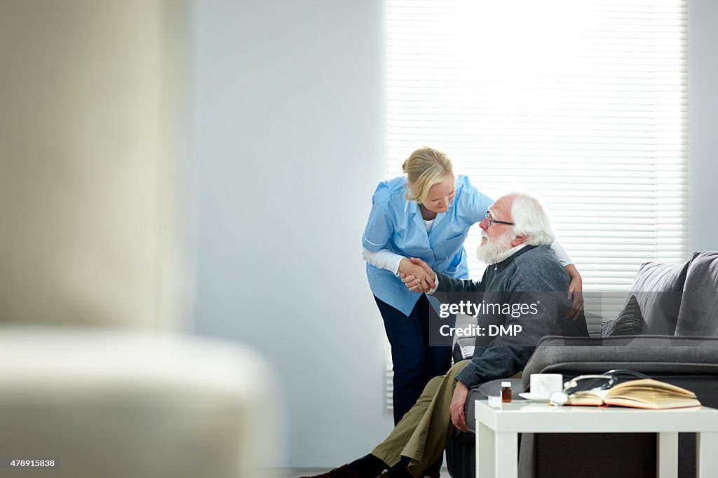 Female caregiver helping senior man get up from couch