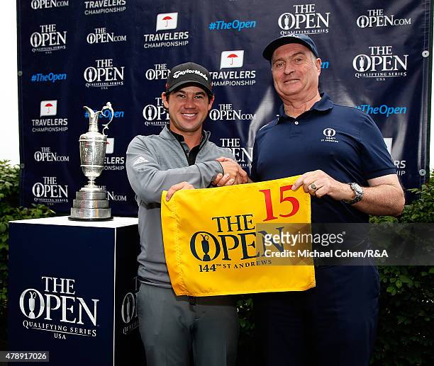 Brian Harman of the United States stands with John Louden of the R & A Championship Committee and the Open Championship Trophy holding a hole flag...
