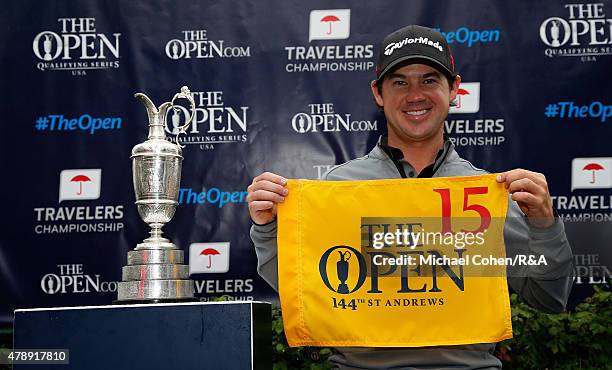 Brian Harman of the United States holds a hole flag and stands next to the Open Championship Trophy after qualifying for the Open Championship during...