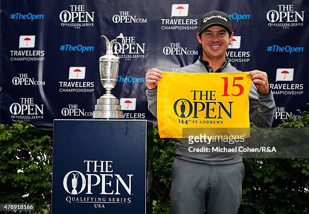 Brian Harman of the United States holds a hole flag and stands next to the Open Championship Trophy after qualifying for the Open Championship during...
