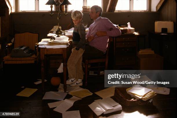 In the paper-strewn writing studio at his summer home, American writer and journalist George Plimpton sits at his desk with his son, Taylor Ames...