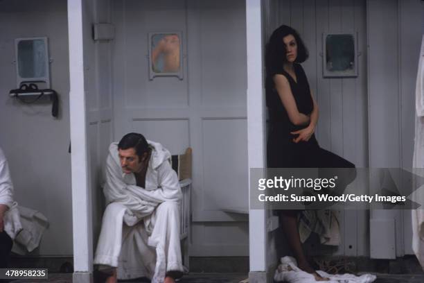Wrapped in a robe, Italian film actor Marcello Mastroianni sits in a changing stall, beside other cast members, in a scene from the film 'Leo the...
