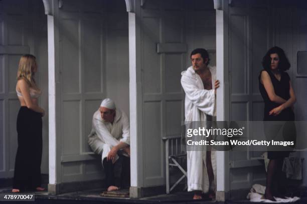 Wrapped in a robe, Italian film actor Marcello Mastroianni stands in a changing stall, as other cast members undress, in a scene from the film 'Leo...