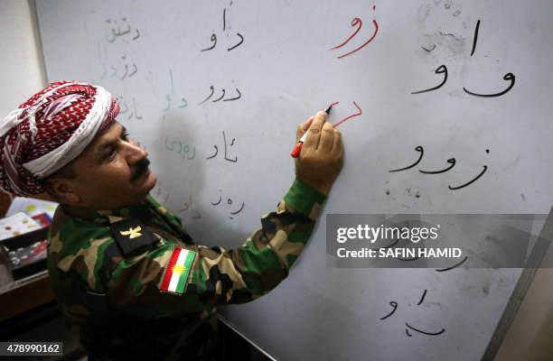 An Iraqi Kurdish peshmerga fighter writes on a white board in Kurdish as he attends a class at a school in the northern Iraqi village of Bahra, east...