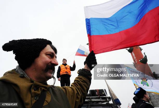 Wearing papakha traditional Cossacks fur hat a man waves a Russian flag to greet an auto-rally in support of the Crimean referendum in Russia's...