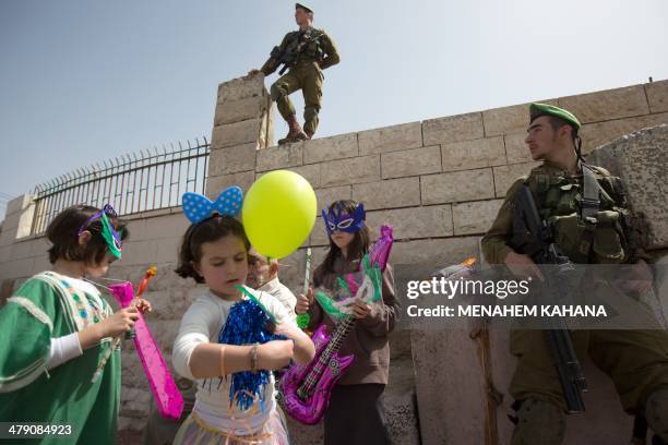 Israeli soldiers secure the area as Israeli settler children dressed up in masks take part in a parade to celebrate the Jewish holiday of Purim in...