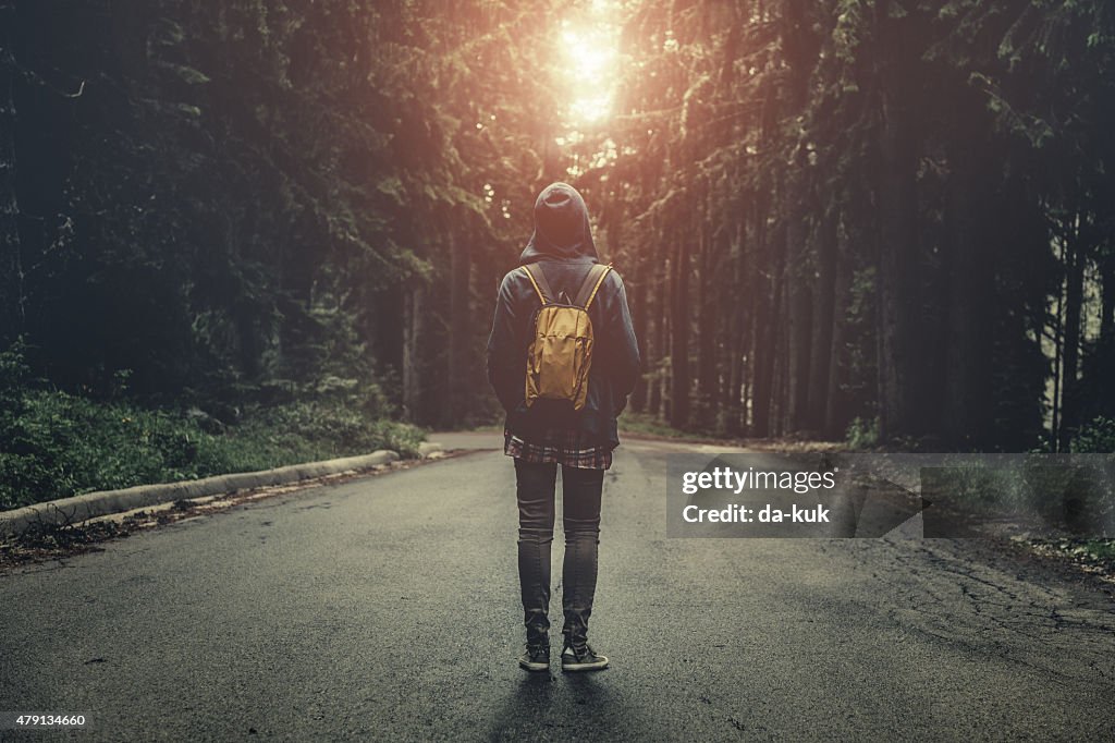 Traveler with backpack walking in a foggy forest at sunset