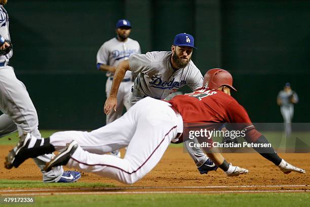 Infielder Scott Van Slyke of the Los Angeles Dodgers reaches to tag out the diving Yasmany Tomas of the Arizona Diamondbacks during the first inning...