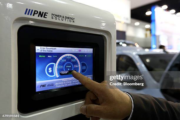 General Motors Co. Chevrolet employee uses the touch screen of a charging stand for the company's Spark electric vehicle at the first International...